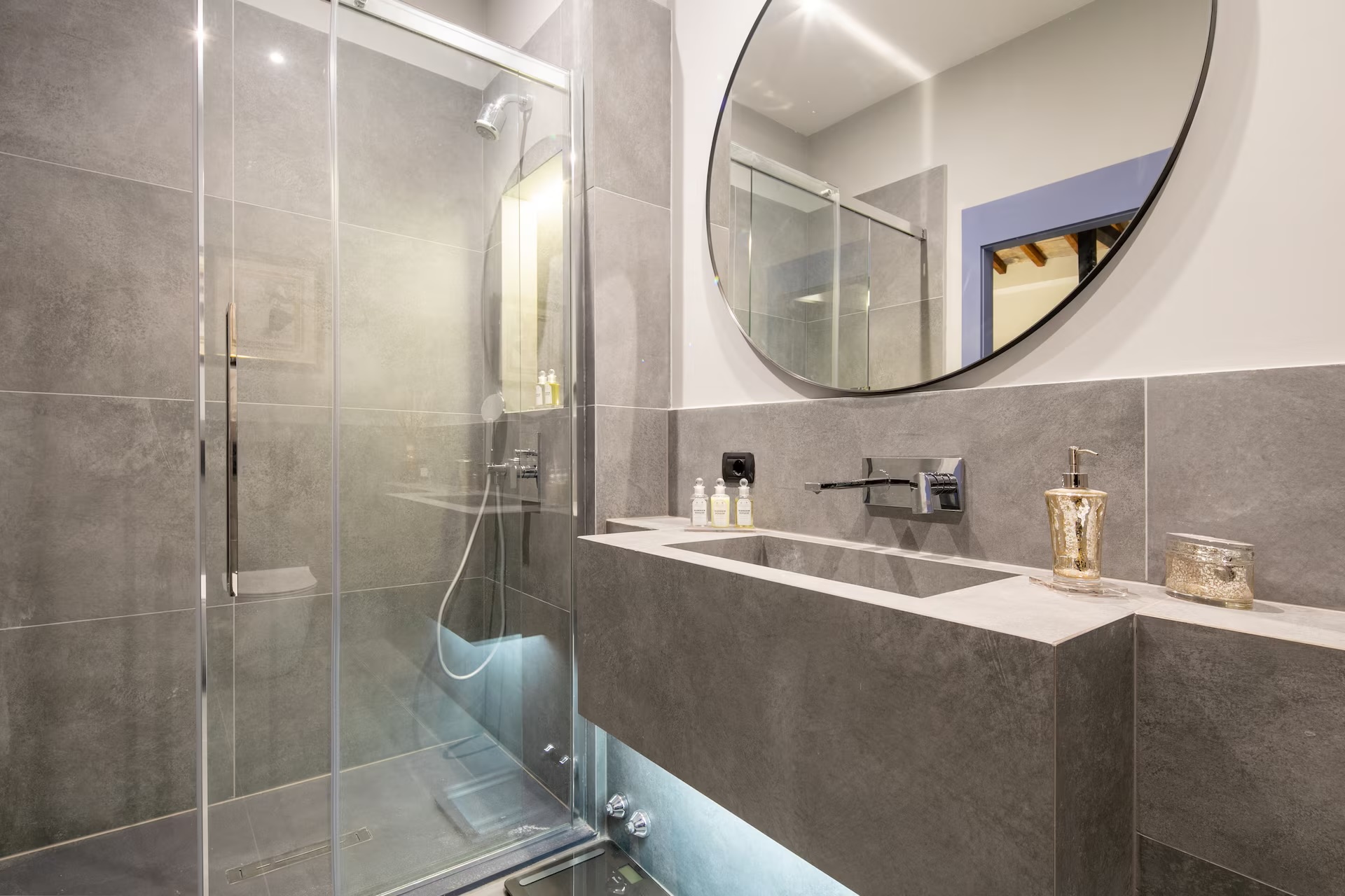 Grey stone bathroom with round mirror and walk-in glass shower